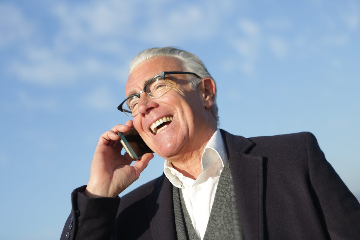 old man in suit wearing his glasses on his phone smiling