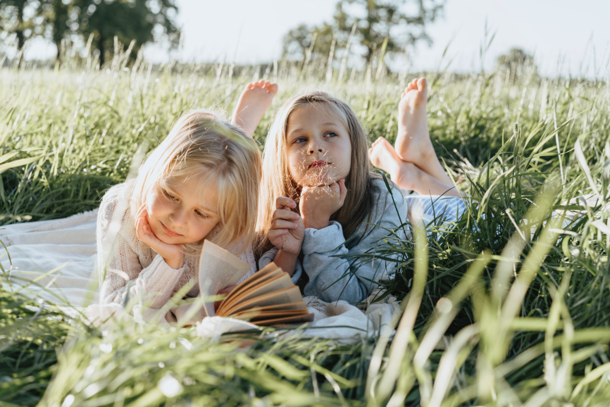 two motivated little girls reading books outdoors