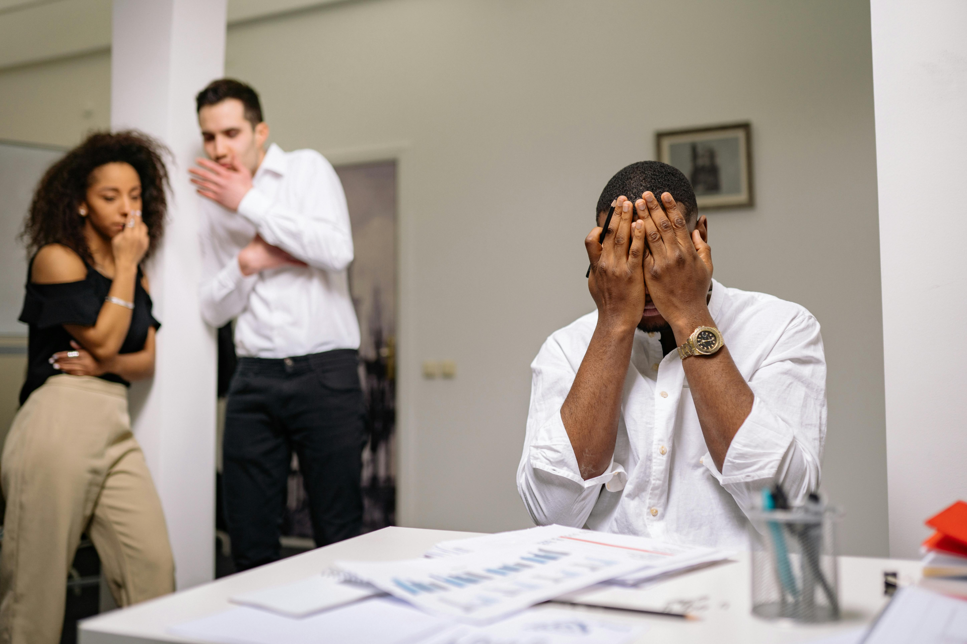 Fear of Success: a man in white shirt covering his face while his colleagues are in the background