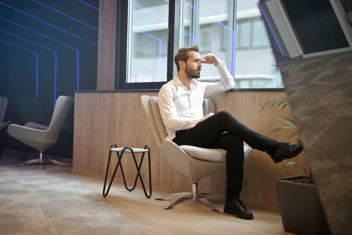 how to silence the mind: a man sitting near a window with his hand on his forehead overthinking