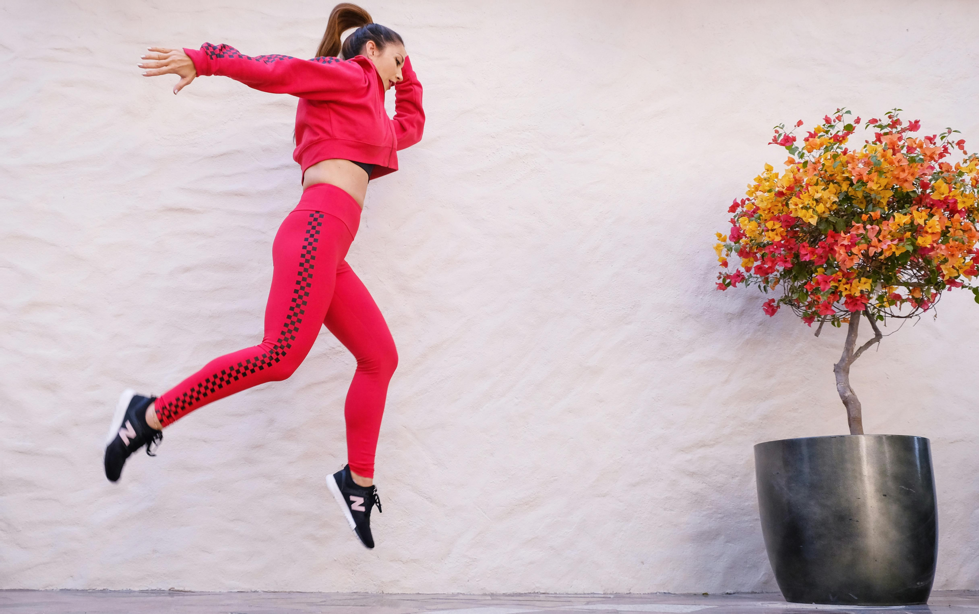 Fitness Attitude: Getting a Workout Mindset: a woman in red yoga pants and red running jacket jumping beside a wall and a potted plant