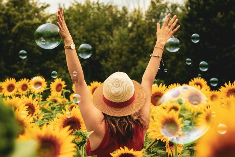 self discovery: a woman on her hat on her back in a sunflower field looking happy