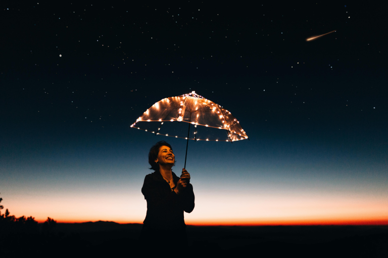 Being happy with less: a woman under a transparent umbrella with lights smiling: