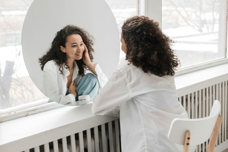 Importance of Self Reflectio :a young woman with curly hair smiling looking herself in the mirror