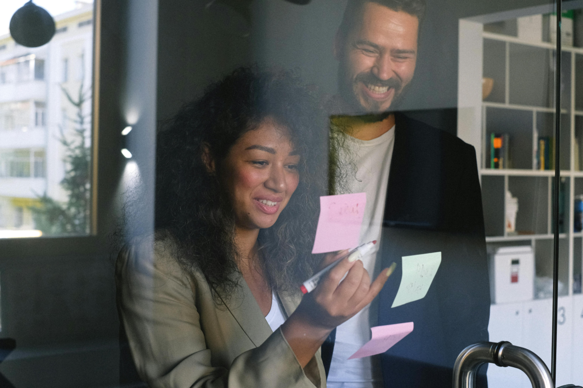 Being Valued At Work: two smiling colleagues looking at sticky notes on the glass wall