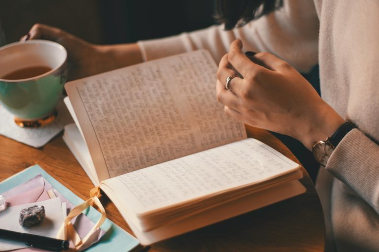 Keeping a personal growth journal : woman reading her journal with a cup of coffee in one hand